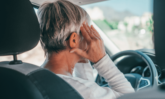 a woman on the driver seat holding her head with both hands.