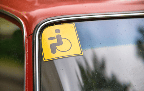 A yellow disability friendly tag on a windshield of a red car.